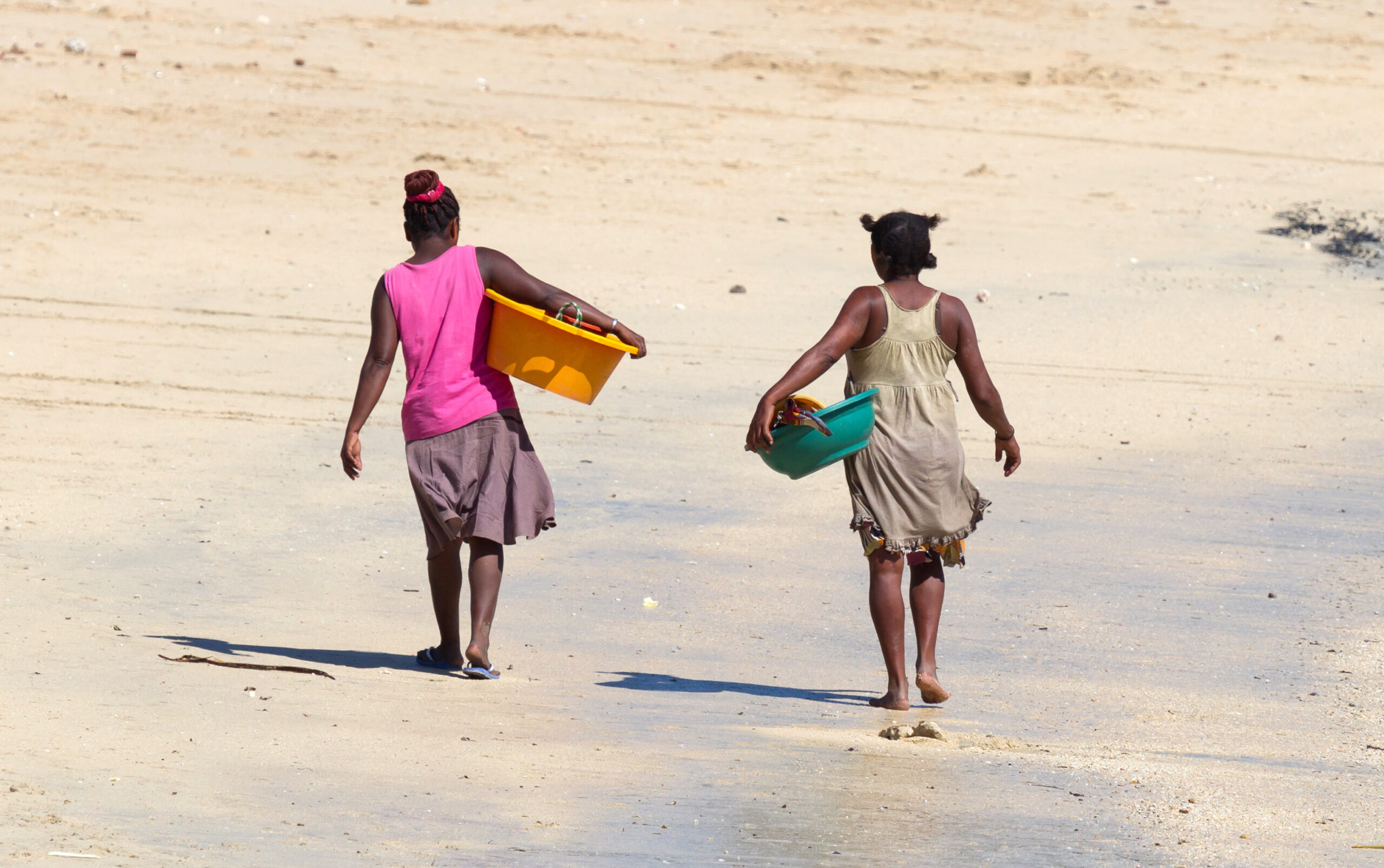 African women walking over the beach with laundry